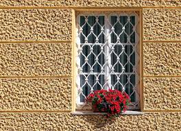 Inferriate Finestra con grata, decorata con un vaso di fiori rossi su una parete gialla.