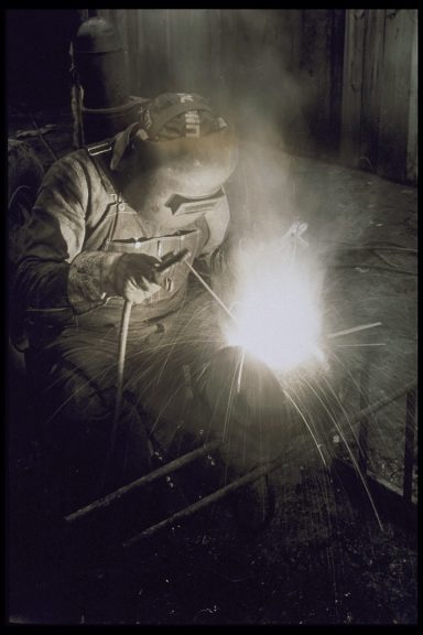 Lavori in Ferro Welder wearing protective gear working on metal, sparks flying.